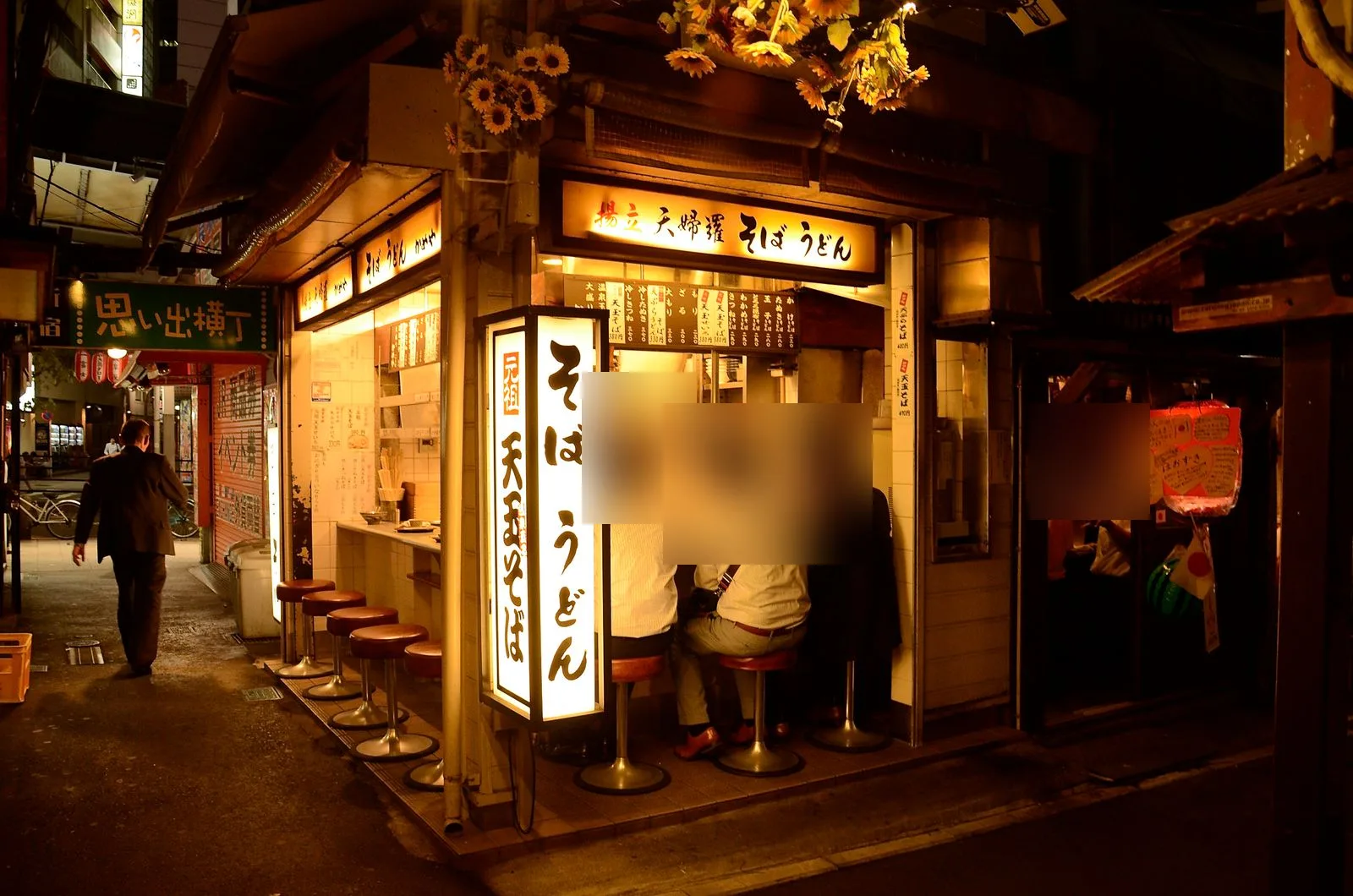 思い出横丁の細い路地に並ぶ小さな飲食店と提灯。写り込んだ人の顔はぼかしている